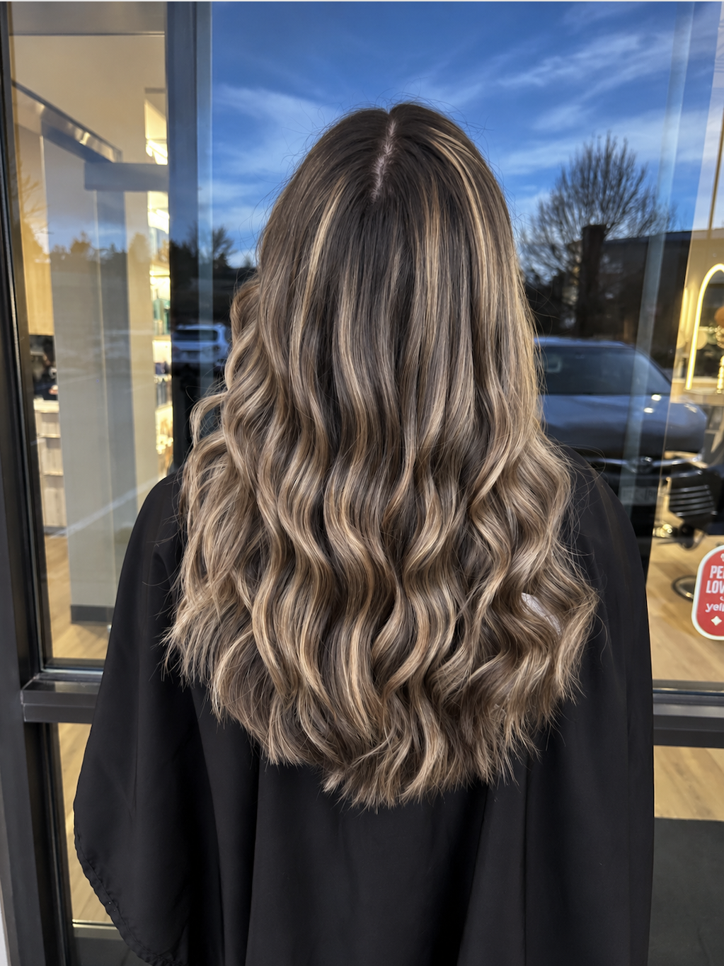 Back view of long brunette hair with soft caramel balayage and loose waves, styled at Kari & Co Hair Studio